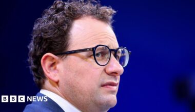 Anthropic CEO Dario Amodei on a stage, furrowing his brow behind round, black-rimmed eye classes.