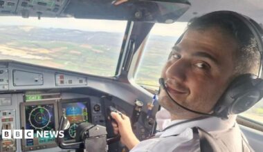Mr Abbasi, sitting in the cockpit of an aircraft in front of the control system. He wears a pilot's shirt and earpiece and is flying the plane in this picture.