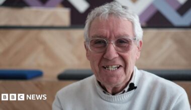 Gregor Fisher. A 72-year-old man with grey hair and glasses. He is wearing a cream jumper and polo shirt, and smiling at the camera.