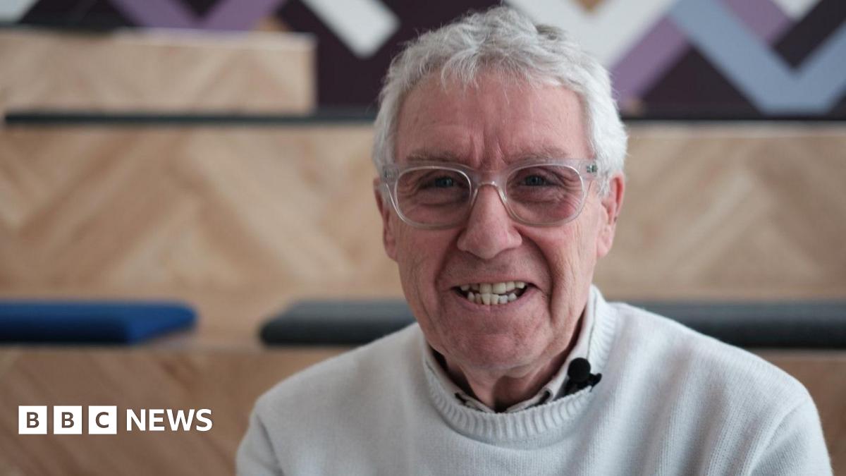 Gregor Fisher. A 72-year-old man with grey hair and glasses. He is wearing a cream jumper and polo shirt, and smiling at the camera.