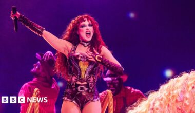 Chappell Roan holding a microphone above her head while performing on stage wearing a corset