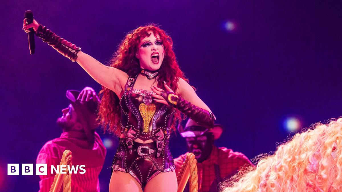 Chappell Roan holding a microphone above her head while performing on stage wearing a corset