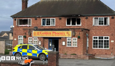 Shot of a fire-damaged building with a police car parked at the front. It has Georgian-style windows and a sign which says Golden Phoenix above the door.