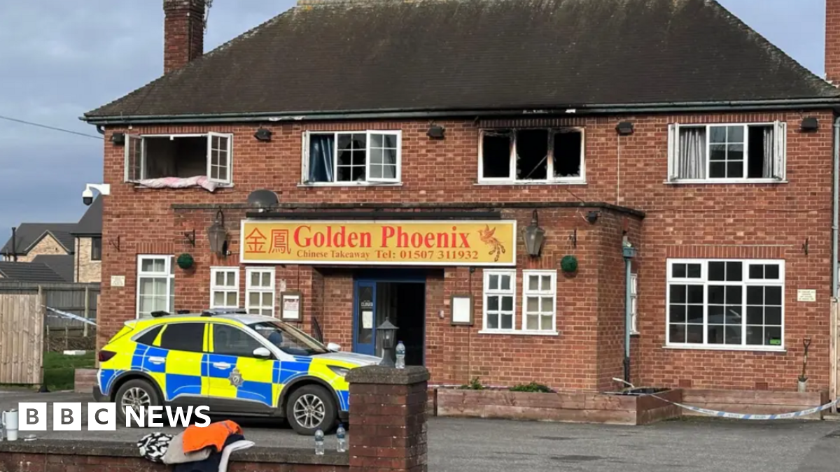 Shot of a fire-damaged building with a police car parked at the front. It has Georgian-style windows and a sign which says Golden Phoenix above the door.