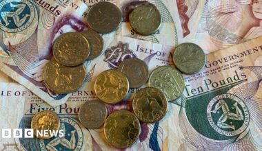 An assortment of Manx 10 and five pound notes, with a collection of coins on top of them - a mixture of pound coins, and small change.