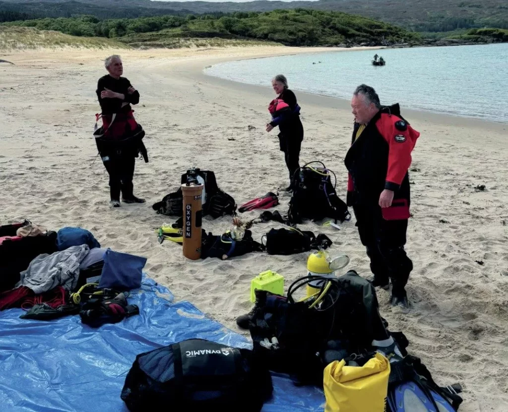 Divers and expedition members preparing equipment on a Scottish beach