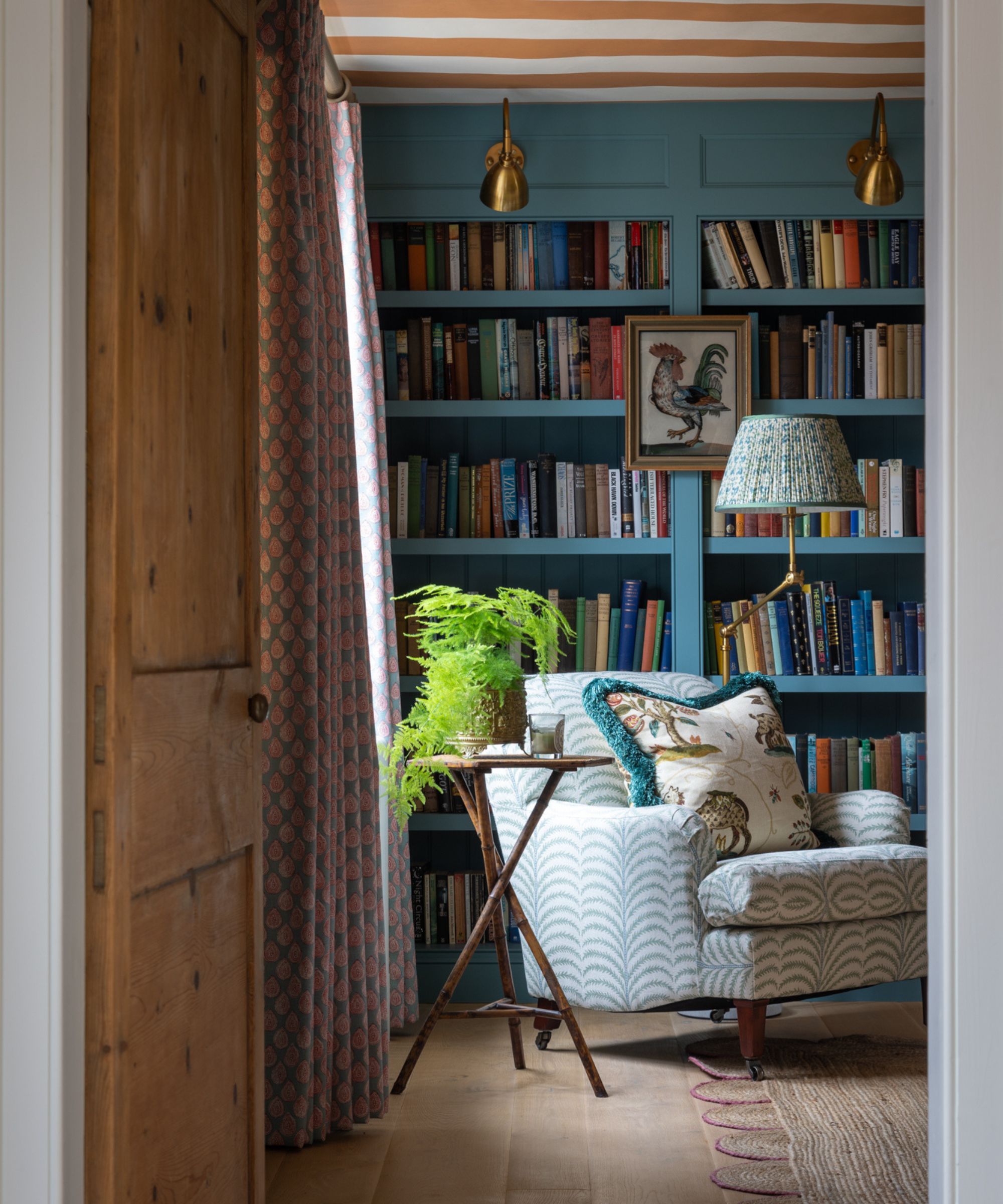 a country home snug room with book built-in bookcases, a striped ceiling, wooden floor, scalloped jute rug and a chair table and floor lamp vignette