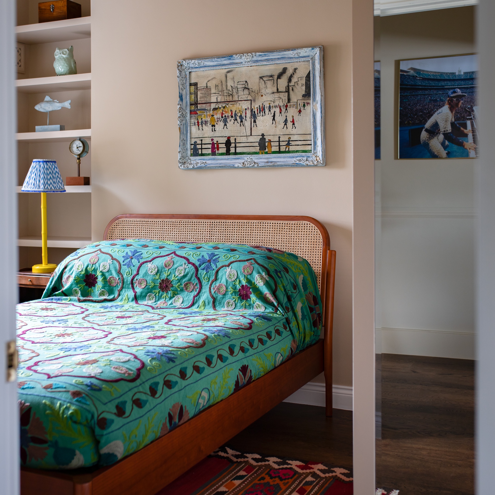 bedroom with pale pink walls, artwork above bed, and embroidered textile throw on bed
