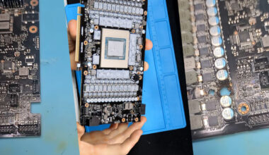 A person holds a disassembled Gigabyte graphics card, showing its exposed circuitry and GPU chip on a blue anti-static mat.