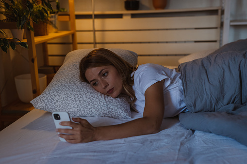 Woman feeling restless and using smart phone on bed at night