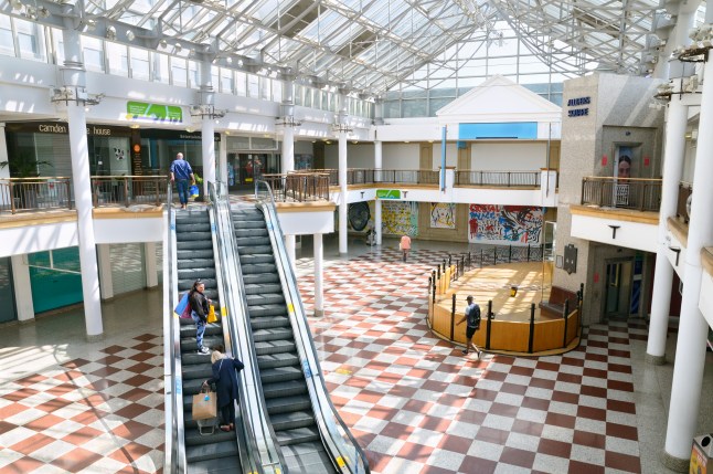 An interior view of Whitgift Shopping Centre in Croydon, which has square patterned flooring and two escalators between the upper and lower levels.