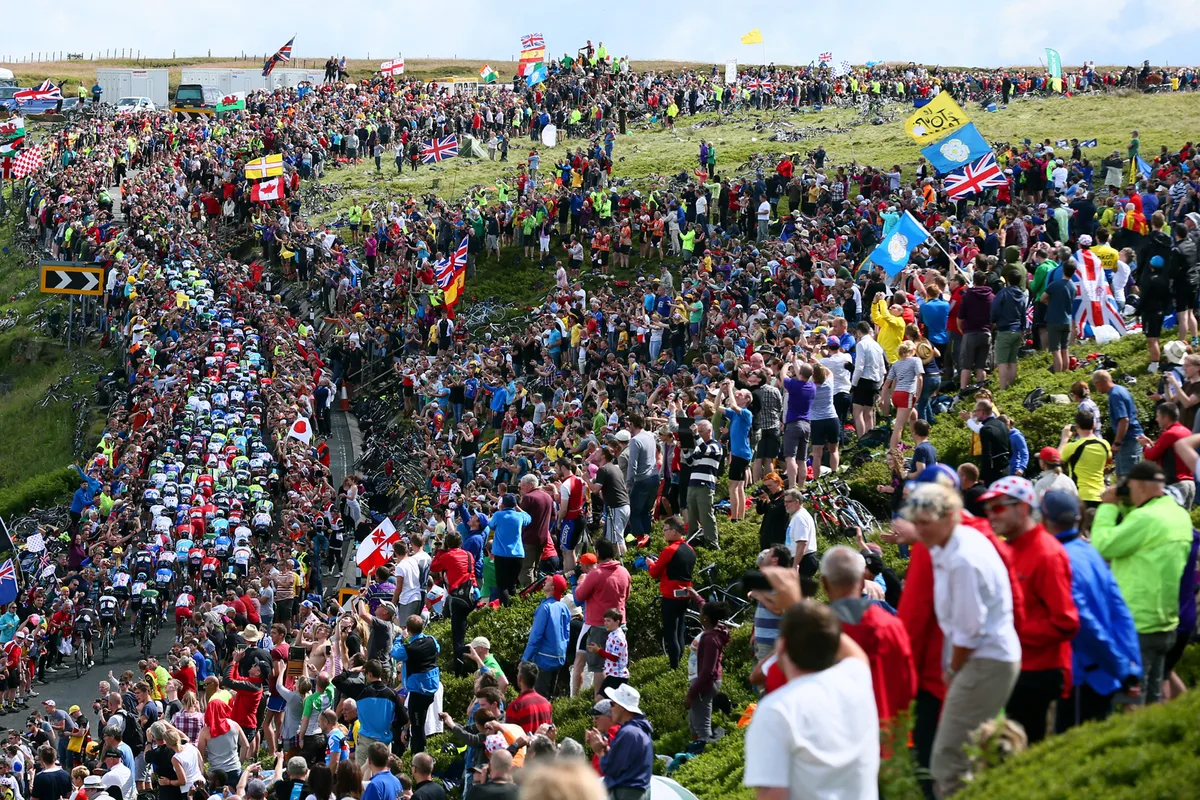 Crowd at Tour de France in Yorkshire as peloton cycles up climb.