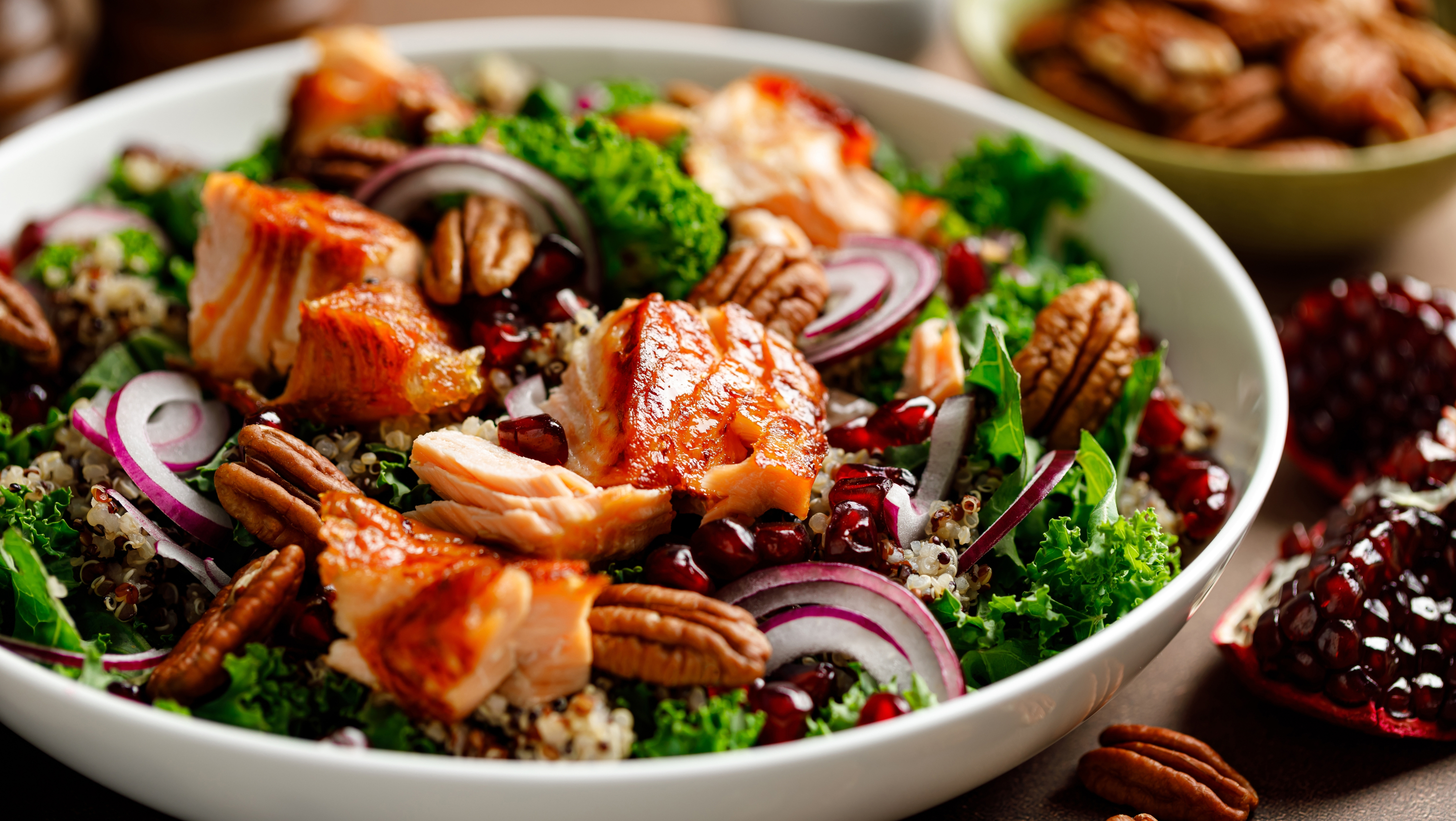 salmon, kale, red onion, pomegranates and pecans mixed together in a bowl