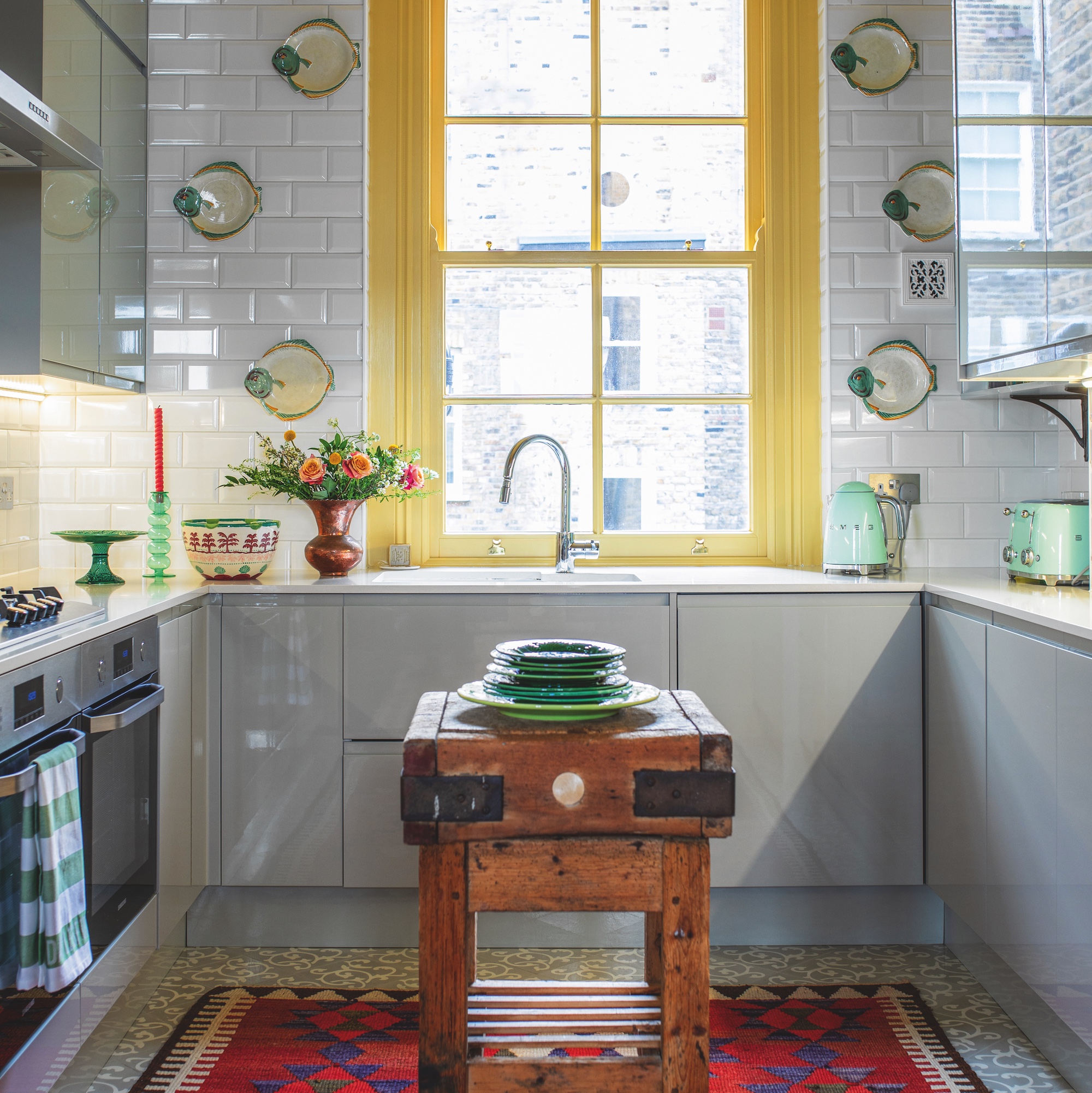 kitchen with yellow painted window fame and white metro tiles on wall with antique butchers block in centre of room