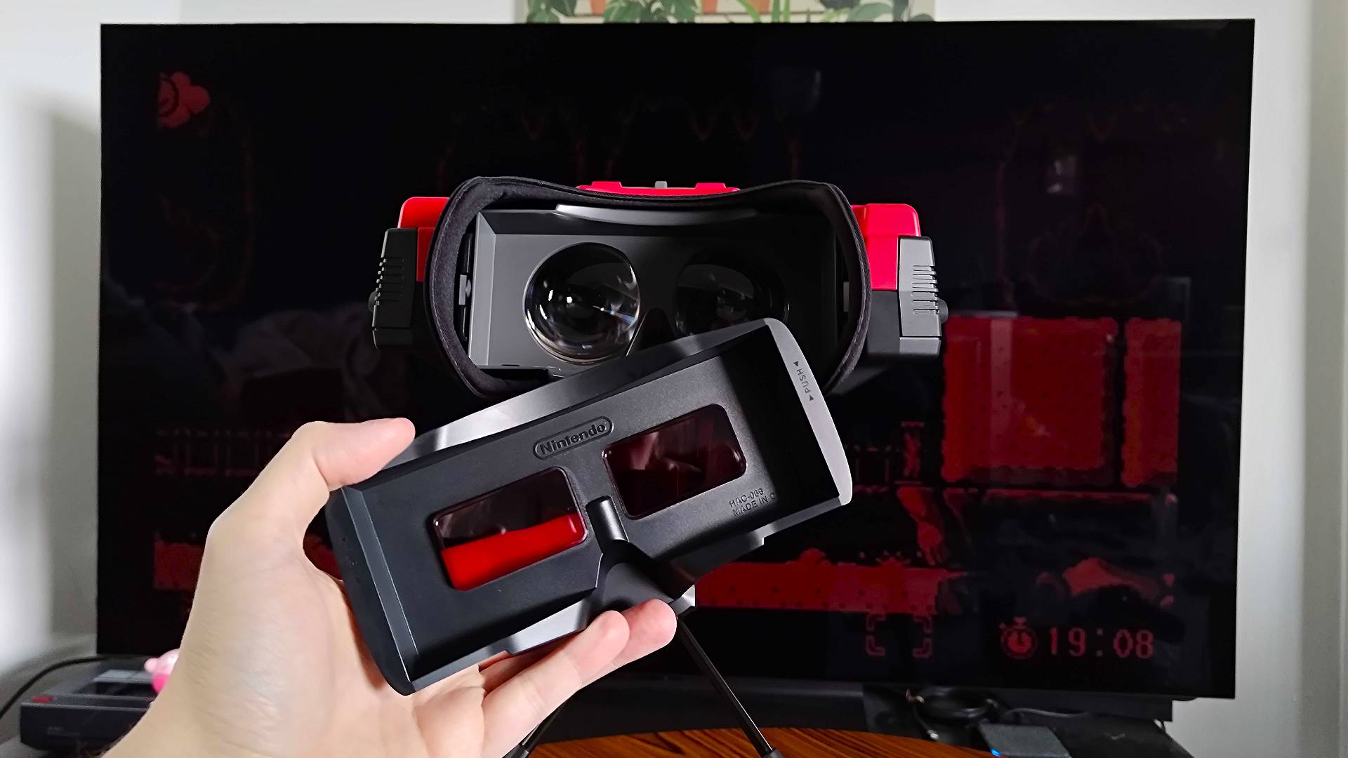 Virtual Boy with hand holding red front lens filter detached from goggles.