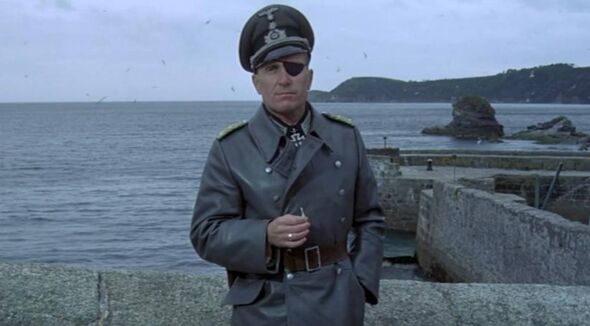 An individual dressed in a military uniform stands at the edge of a concrete platform, overlooking a body of water with a distan An individual dressed in a military uniform stands at the edge of a concrete platform, overlooking a body of water with a distan