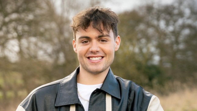 Bradley Riches posing as Emmerdale character Lewis Barton, smiling.