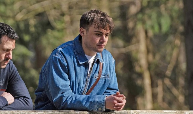 Emmerdale's Lewis Barton resting his arms on a stone wall and looking dejected.