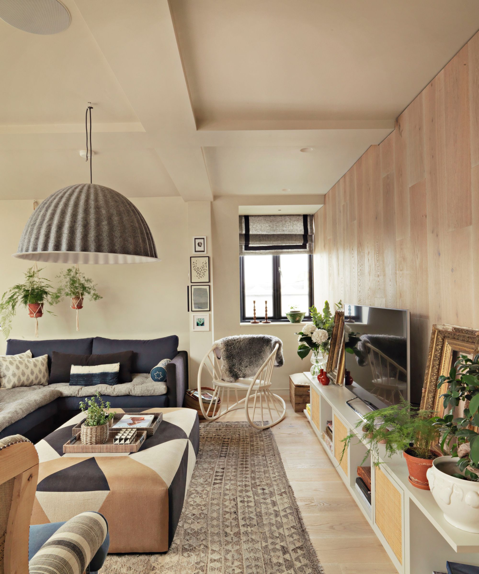 Scandi style living room with large rug, ottoman, rocking chair with sheepskin throw, low pleated pendant light and wooden wall
