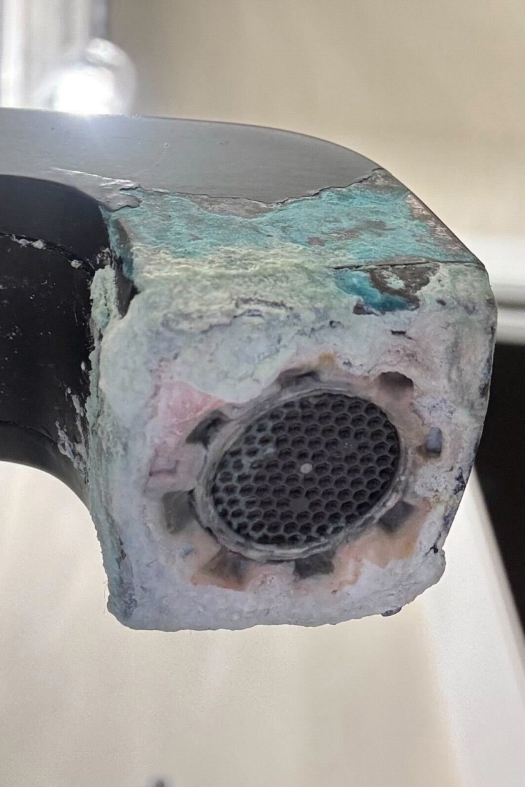 A view looking up from under a faucet, which has an uneven surface covered with white, pink, blue and yellow residue.