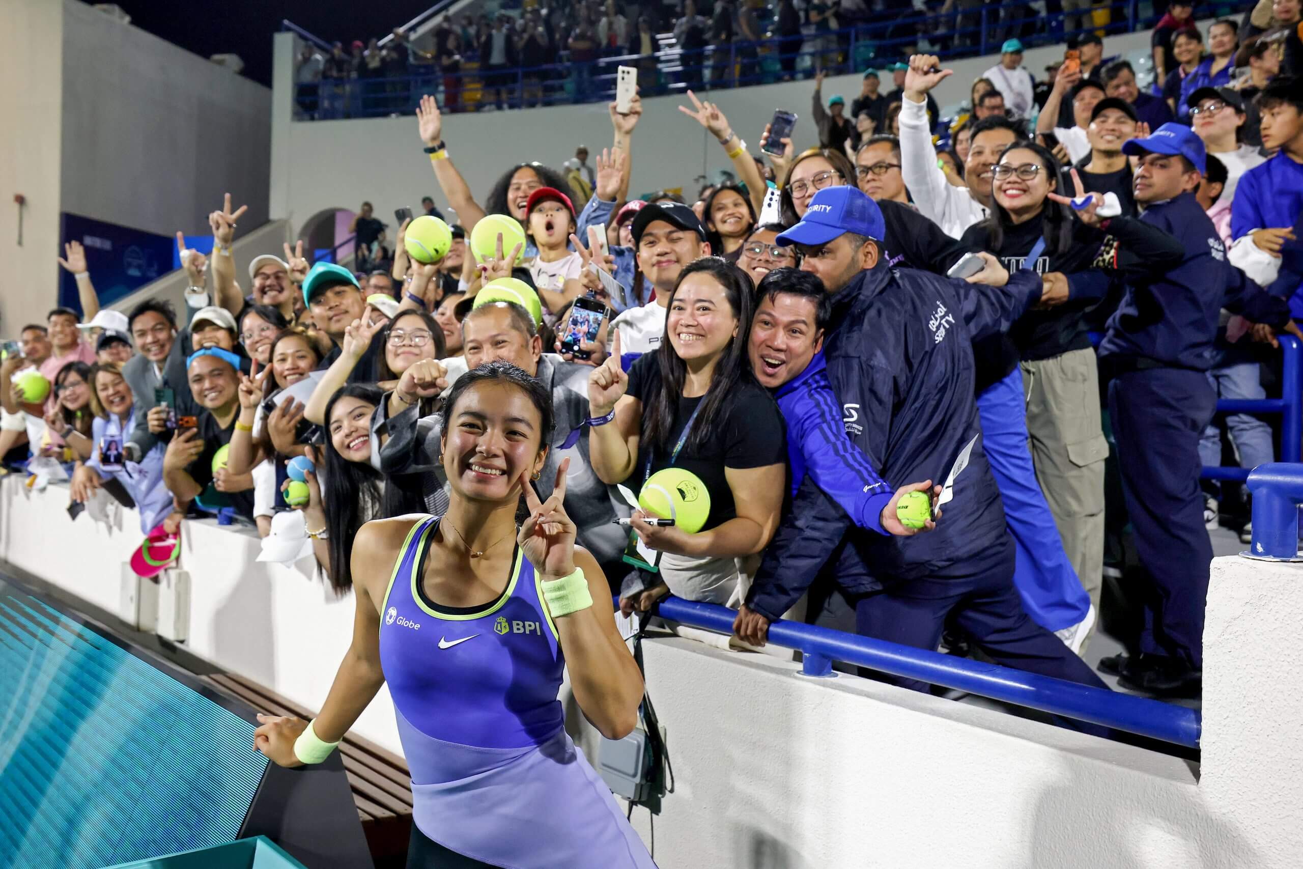Alex Eala does a peace sign while posing for a photo in front of Filipino tennis fans.