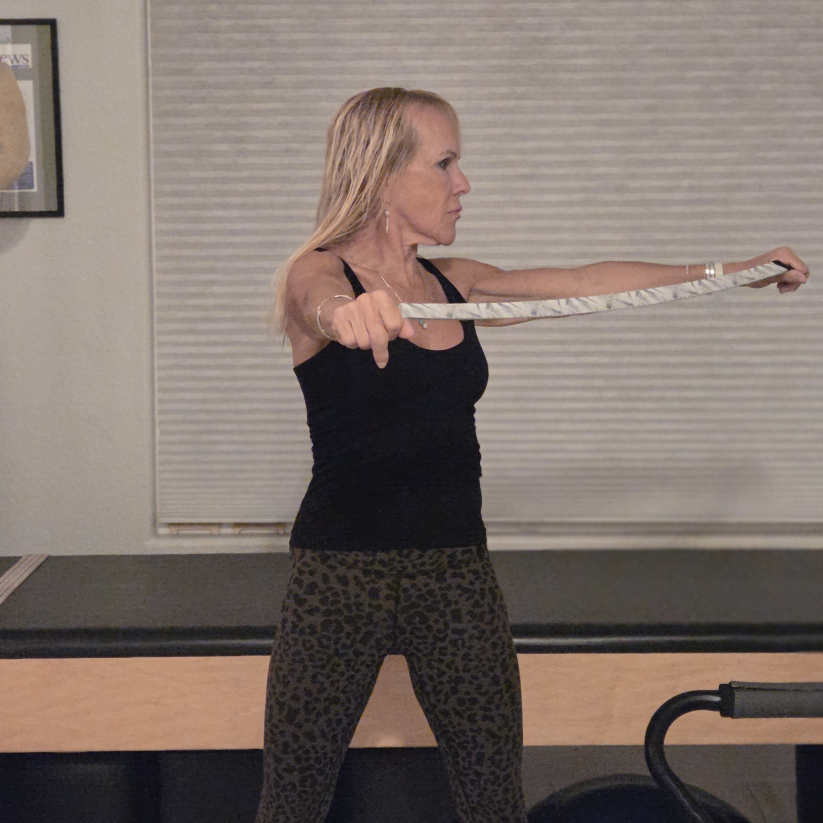 Woman stretching with yoga strap in front of a Pilates reformer bed