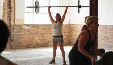 Woman lifting barbell above head with weight on either side wearing gym clothes and standing with friends in foreground
