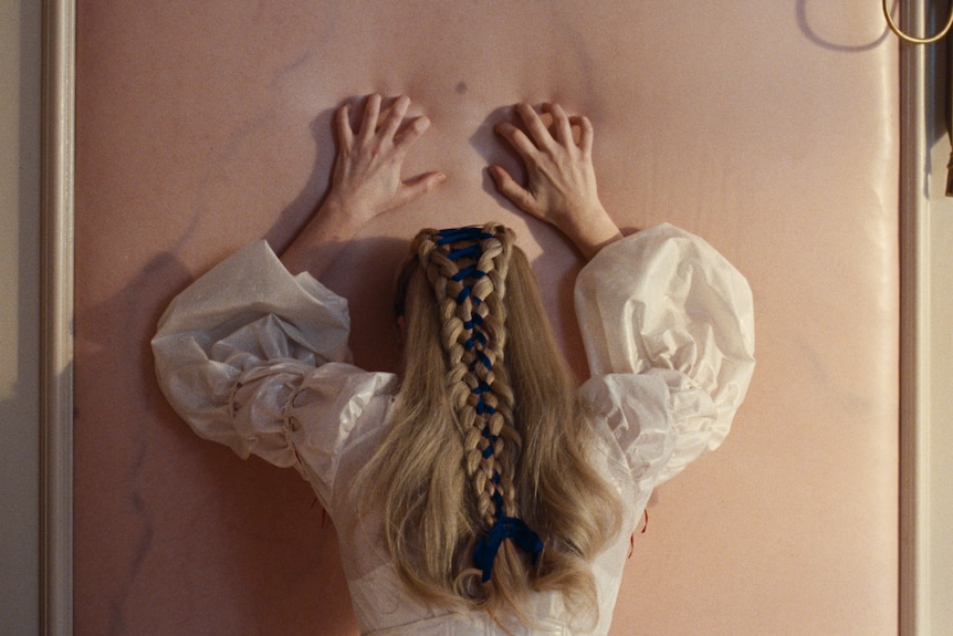 A woman runs her hands down a flesh coloured wall.