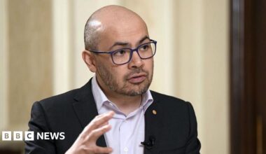 A fossil of part of a crinoid that resembles a row of teeth. The markings form a curved shape with pale, tooth‑like segments set against the darker surface of the fossil. The fossil rests on another rock in the foreground.