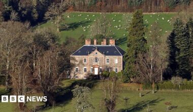 Torwoodlee House in the Borders - an impressive brick building with a number of chimneys nestled between trees with farmland around
