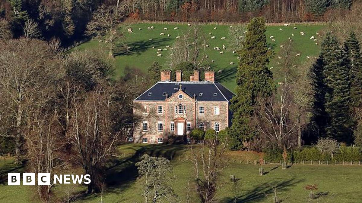 Torwoodlee House in the Borders - an impressive brick building with a number of chimneys nestled between trees with farmland around