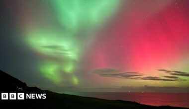Green and pink skies are reflected in the sea and the headland is in silhouette.