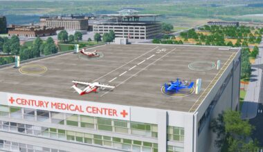 An artist’s concept image shows the square, gray rooftop of a hospital building with three concept aircraft sitting on top. One aircraft is painted dark blue, and two are painted with red and white paint schemes. Each aircraft has several unique propellors and wings to showcase that these aircraft can take off and land on short runways or vertically. The words “Century Medical Center” – in red – sit below the rooftop landing pad with several rows of windows underneath. In the background, there are several rows of trees, buildings, and parking garages, to show that this building is inside of a city.