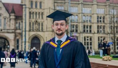 Chris Bartley, a man with brown hair and stubble, he wears glasses and a graduation cap and gown in front of a large university building.