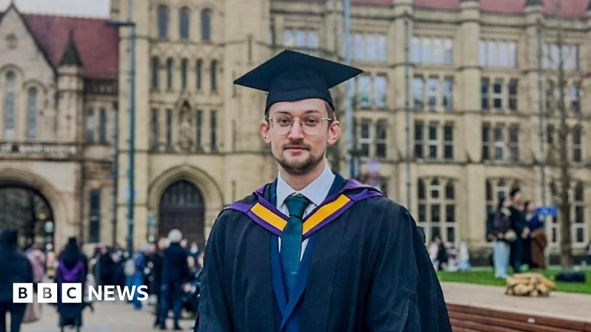 Chris Bartley, a man with brown hair and stubble, he wears glasses and a graduation cap and gown in front of a large university building.