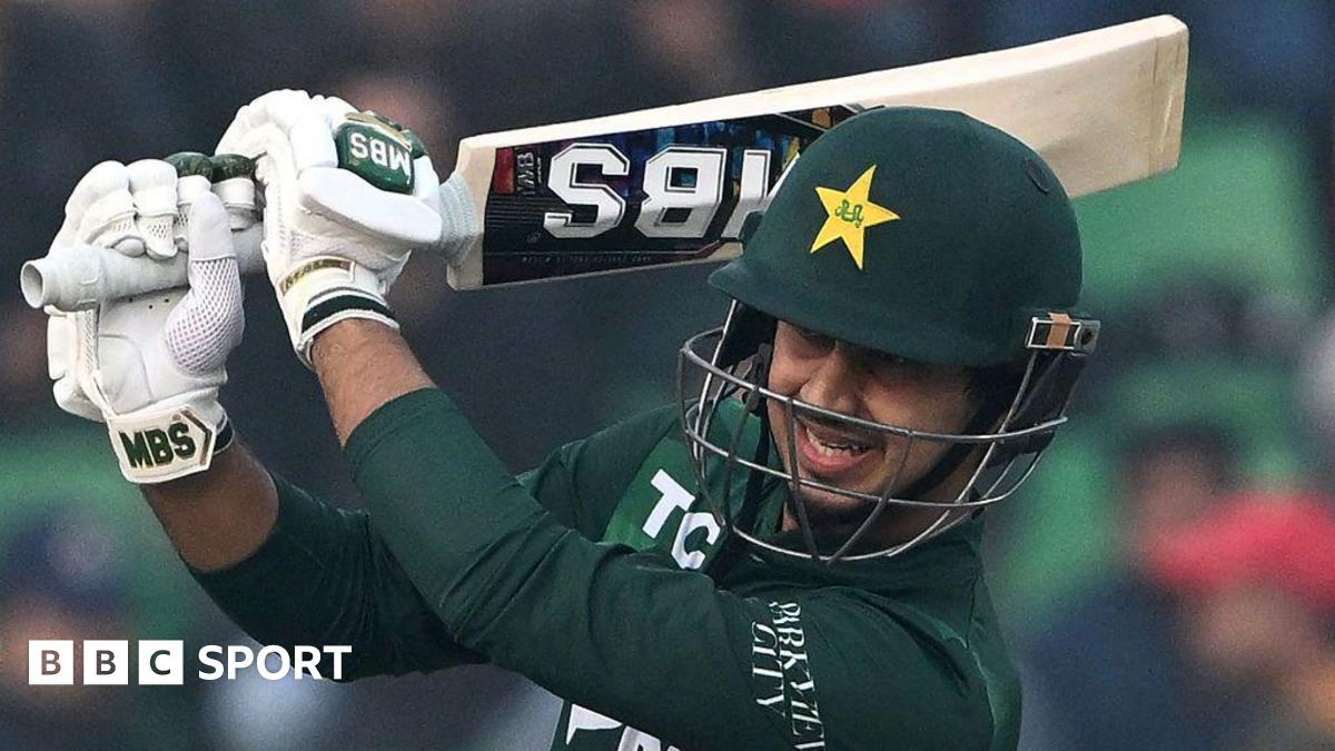 Pakistan's Saim Ayub plays a shot during the third T20 international cricket match between Pakistan and Australia. He is wearing a green helmet that has a wire face guard. His shirt is also dark green while his gloves are white. His bat is raised up around his head.