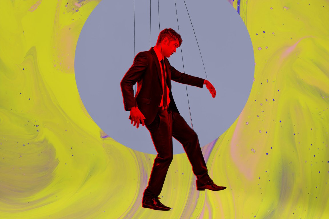 A man in a black suit and tie is depicted as a marionette puppet, suspended by strings. He is highlighted with a red outline and positioned against a large gray circle on a vibrant yellow and purple marbled background.