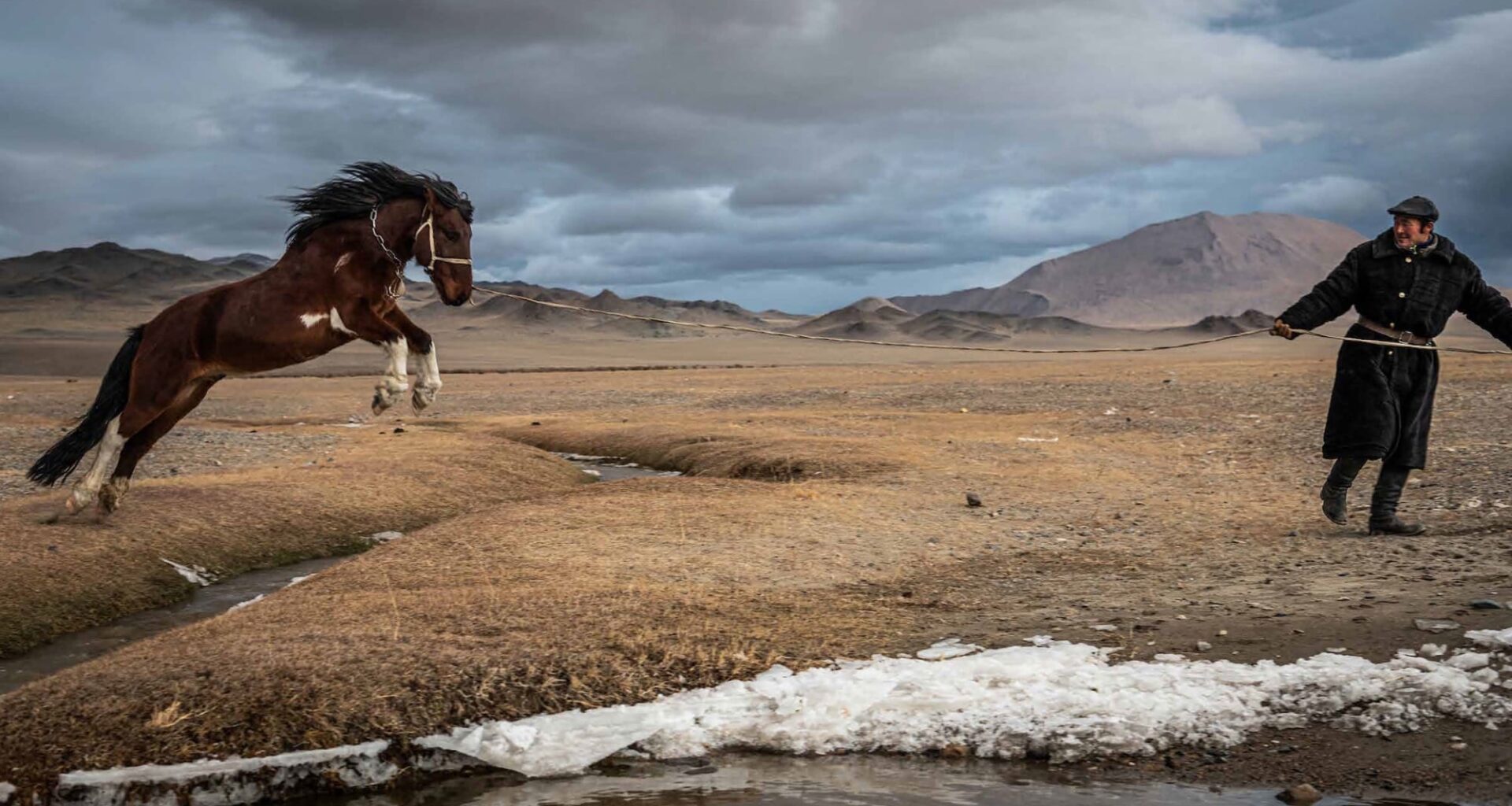 A photograph by Claire Thomas of a Kazakh man encouraging a large horse to leap over a stream