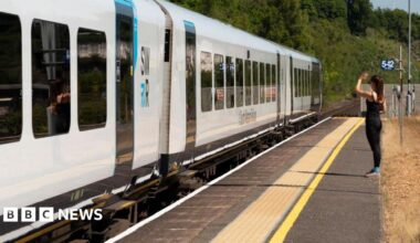 A woman waving from platform as a white South Western Railway passenger train departs Micheldever Station.