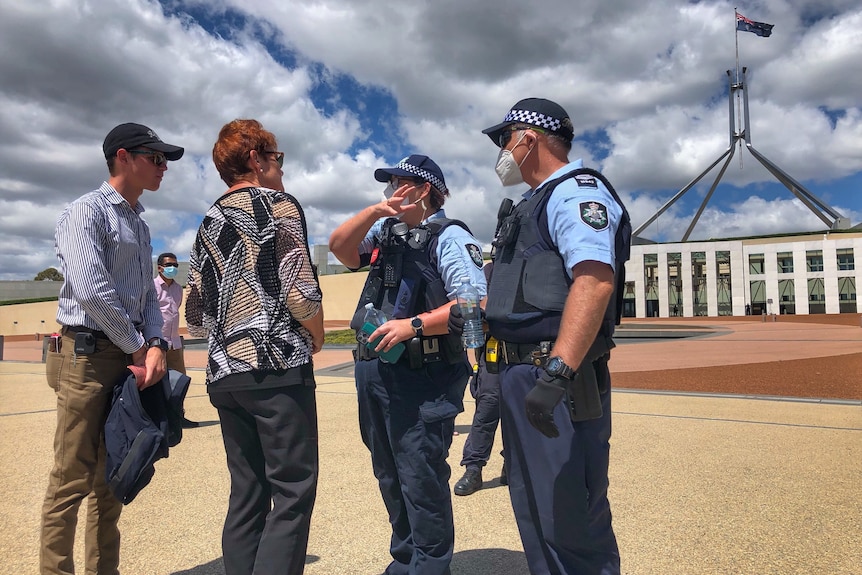 Two uniformed officers talk to Pauline Hanson outside Parliament House.
