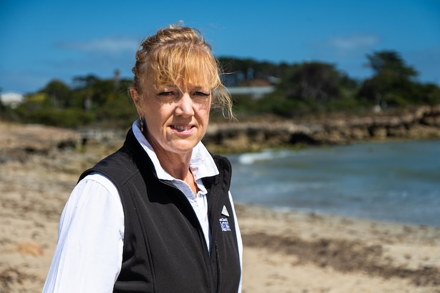 A woman in a white shirt with a black vest on a beach