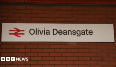 A train station sign reading 'Olivia Deansgate' hangs on a red brick station wall