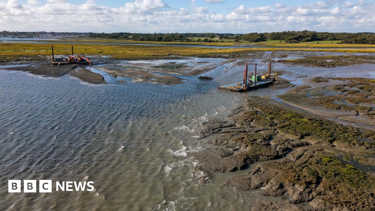 A shot of the restoration work being done at Lymington. Equipment can be seen set up on mud next to a body of water.