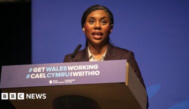Kemi Badenoch stood at a lectern that reads "#Get Wales Working" in Welsh and English.