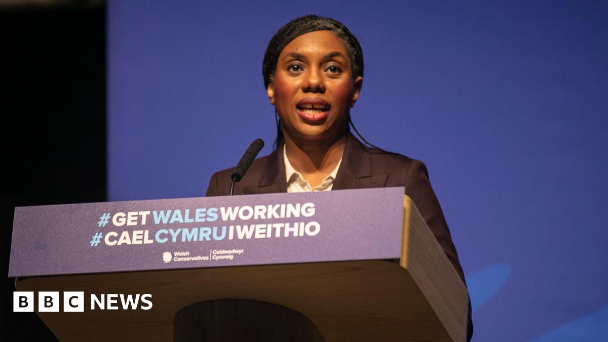 Kemi Badenoch stood at a lectern that reads "#Get Wales Working" in Welsh and English.