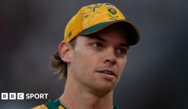 A close up of Tristan Stubbs' face as he looks on, the background is blurred and he is wearing a yellow South African Cricket cap. His cap number is 95.