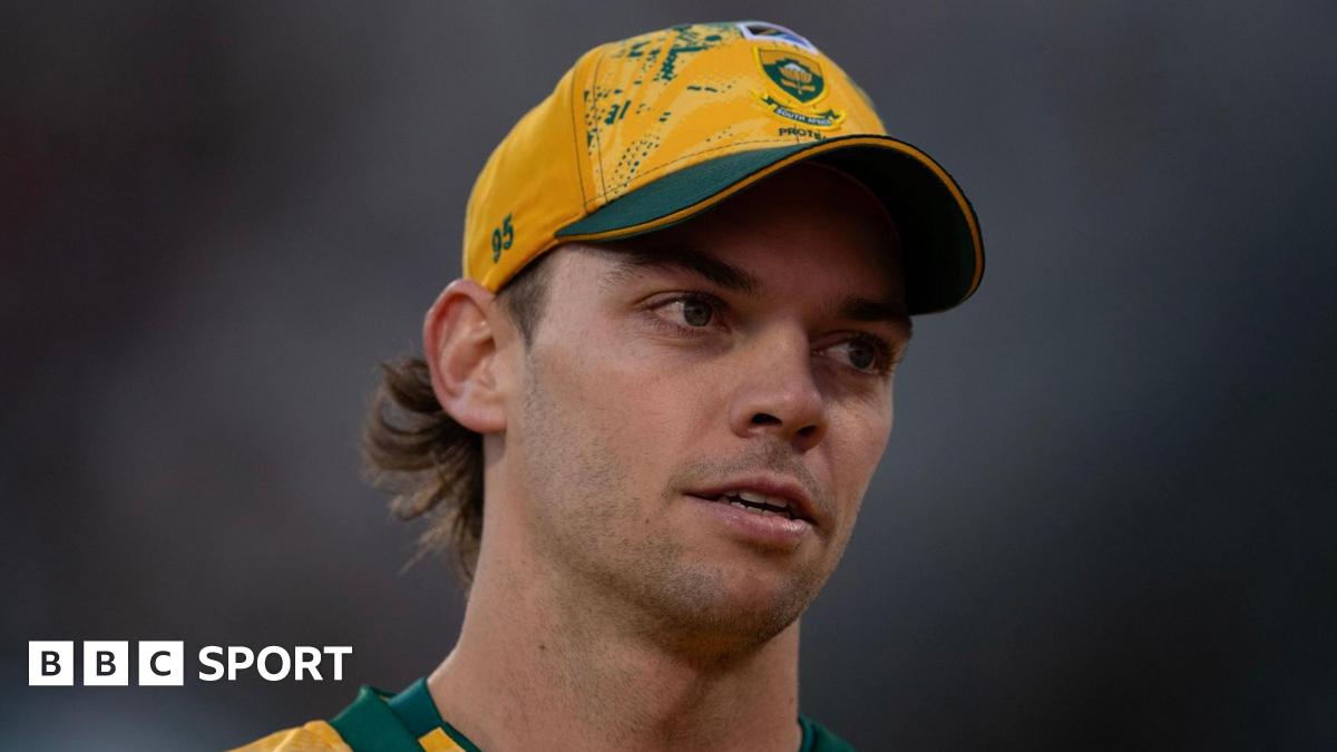 A close up of Tristan Stubbs' face as he looks on, the background is blurred and he is wearing a yellow South African Cricket cap. His cap number is 95.