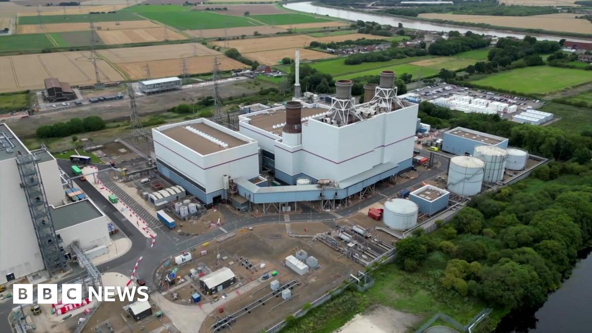 Aerial view of the power station at Keadby in North Lincolnshire. There is a large central white building with smaller buildings around the perimeter of the site. There are trees and farmland in the background.