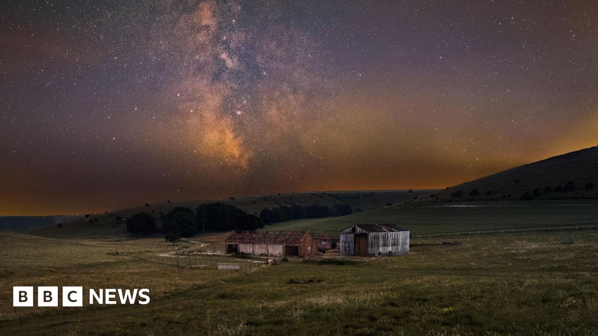 An abandoned barn in a field lit by the night sky.