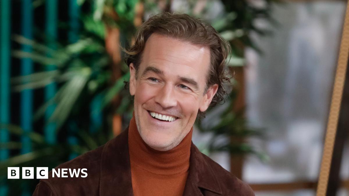 James Van Der Beek dressed in an orange turtleneck and chocolate coloured blazer.
